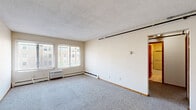 Located at 414 Erie St SE in Minneapolis, Minnesota, this two-bedroom, one-bathroom unit offers a practical and well-organized single-floor layout. The living area is generously proportioned, featuring wall-to-wall carpet, a textured ceiling, and a large window with blinds that allows natural light to fill the space. A baseboard heating unit and a wall-mounted AC unit ensure year-round comfort. The kitchen is efficiently designed with warm wood cabinetry, light countertops, tile flooring, and white appliances including a refrigerator, electric range, and dishwasher, along with a double sink beneath additional upper cabinets. Both bedrooms are carpeted and feature natural light from windows with blinds and baseboard heating. The primary bedroom offers generous proportions, while the second bedroom is equipped with a wide set of double bi-fold closet doors, providing substantial storage. The full bathroom includes a tiled tub-shower combination with a sliding glass door enclosure and a clean, functional layout. A connecting hallway with additional closet access ties the rooms together efficiently, making this a well-appointed and organized living space.
