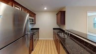 This single-floor residence offers a thoughtfully designed layout that balances open communal spaces with comfortable private quarters. The entry leads into a combined living and dining area, where light hardwood flooring transitions seamlessly into plush wall-to-wall carpeting. Recessed lighting and a sliding glass door with vertical blinds flood the living space with natural light, while a large window frames outdoor greenery views.

The kitchen is a functional highlight, featuring rich medium-toned wood cabinetry, dark granite countertops, and a full suite of stainless steel appliances including a refrigerator, microwave, and range. A breakfast bar with countertop overhang connects the kitchen to the main living area, enhancing the open-concept feel.

The bedrooms are carpeted and finished with warm neutral tones. Each room features windows with blinds that allow for ample natural light. The layout also provides convenient access to a full bathroom equipped with a tub-shower combination, wood vanity, and white countertop, as well as a second bathroom featuring a separate shower stall and similar finishes. Clean white doors, consistent trim work, and a cohesive neutral color palette unify the overall aesthetic throughout the space.