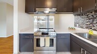 This single-floor unit offers a well-organized layout with a bright, open living area anchored by warm hardwood-style flooring and large windows dressed with vertical blinds that invite generous natural light. The living space connects seamlessly to the kitchen through a open doorway, creating an easy flow between rooms.

The kitchen is a functional highlight, featuring dark espresso cabinetry contrasted by light quartz-style countertops and a mosaic tile backsplash in neutral tones. A stainless steel electric range with overhead ventilation hood serves as a centerpiece, while tile flooring and ample upper and lower cabinet storage complete the space.

The bedrooms are comfortably sized, each equipped with ceiling fans and windows with vertical blinds providing outdoor views and natural light. One bedroom features mirrored sliding closet doors with built-in shelving, while additional bedrooms are finished with plush carpeting for comfort.

Two bathrooms offer clean, functional designs with white cabinetry, wide vanities, large mirrors, and tile flooring. The overall ambiance throughout is light and neutral, with textured ceilings, white trim, and a cohesive color palette creating a calm, move-in ready environment.