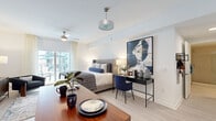 Located along South Dixie Highway in Miami's Coconut Grove area, this one-bedroom, one-bathroom residence offers a thoughtfully designed open-concept layout that maximizes every inch of its compact footprint. Light-toned hardwood-style flooring runs throughout, complementing the crisp white walls and contributing to a clean, contemporary aesthetic.

The main living area seamlessly integrates the kitchen, dining, and sleeping zones. The kitchen is outfitted with stainless steel appliances, including a full-size refrigerator, range, and microwave, alongside taupe cabinetry that extends to the ceiling for ample storage. A wooden bar-height island doubles as a dining surface, providing practical space for meals and entertaining.

The sleeping area is generously proportioned and benefits from large sliding glass doors leading to a private balcony, allowing abundant natural light to filter in. A ceiling fan overhead ensures year-round comfort. The space accommodates a full workspace with room for a desk and seating area.

The bathroom features a glass-enclosed walk-in shower with floor-to-ceiling subway tile, mosaic tile flooring, and a wall-mounted vanity. The overall ambiance throughout the residence is modern and bright, well-suited for urban living in Miami.
