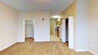 This single-floor residential unit offers a straightforward, functional layout designed for comfortable everyday living. The main living area is finished with wall-to-wall carpet, creating a warm and inviting atmosphere, while neutral-toned walls contribute to a clean, understated aesthetic throughout.

A notable feature of the living space is direct access to a walk-in closet, providing generous storage with a built-in hanging rod system. Adjacent to the living area, the kitchen is efficiently arranged with warm wood cabinetry, a full-size refrigerator, a range with overhead microwave, and ample counter space. The kitchen transitions to a tiled floor, clearly delineating it from the carpeted living zone.

Ceiling-mounted flush lighting provides consistent illumination throughout, complemented by a fire safety system visible in the main area. The entry door is accessible directly from the kitchen corridor, offering a practical flow through the unit. An additional closet or utility space is also present near the kitchen, adding further storage options. Overall, the space is thoughtfully laid out for ease of use, with each area flowing naturally into the next.