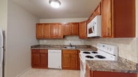 This single-floor residence offers a practical and comfortable layout designed to maximize livable space. The kitchen serves as a functional highlight, featuring rich warm-toned wood cabinetry with brushed metal hardware, granite-patterned countertops, and a neutral tile backsplash. White appliances — including an electric range, built-in microwave, and dishwasher — are seamlessly integrated, while light tile flooring ties the space together with a clean, polished look.

The living area is generously sized, with soft wall-to-wall carpeting underfoot and neutral painted walls that create a bright, open atmosphere. Multiple windows allow natural light to fill the room, with views of the surrounding neighborhood. A wall-mounted air conditioning unit provides year-round comfort, complemented by baseboard heating throughout the unit.

The bedroom spaces continue the same warm, neutral palette with plush carpeting and ample closet storage. Each room benefits from natural light through well-placed windows and offers enough space to accommodate a variety of furniture arrangements.

The bathroom maintains a clean, minimalist aesthetic with white tile walls and flooring, a vanity, and a toilet — all presented in a bright, easy-to-maintain finish. Overall, the residence offers a cohesive, move-in ready environment with practical features throughout.