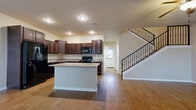 This two-story home offers a well-designed layout across both levels, combining functional living spaces with comfortable finishes throughout. The main level opens with a welcoming entryway featuring warm hardwood-style flooring and a classic arched front door flanked by a window that brings in natural light. The open-concept kitchen is a standout feature, showcasing rich dark wood cabinetry, granite countertops, black appliances including a refrigerator, gas range, and built-in microwave, and a central island that provides additional workspace and storage. A staircase with a sleek black metal railing rises from the main living area, leading to the upper floor. A secondary living or dining area on the main level also features hardwood-style floors and a large window overlooking the exterior. The upper level includes carpeted bedrooms, each offering ceiling fans, natural light through slatted blinds, and generous closet space with mirrored sliding doors. A full bathroom upstairs features a dark wood vanity with granite countertops, a framed mirror, and a tiled tub-shower combination. The attached garage provides practical storage and parking space with an automatic opener. Neutral wall tones and consistent finishes create a cohesive, move-in ready atmosphere throughout the home.