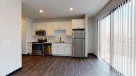 This single-floor unit in Fitchburg, Wisconsin offers a thoughtfully designed layout with modern finishes throughout. The kitchen serves as a central highlight, featuring white shaker-style cabinetry extending to the ceiling for generous storage, granite countertops, and a classic subway tile backsplash. A full suite of stainless steel appliances—including a refrigerator, range, dishwasher, and microwave—adds a sleek, contemporary feel. A large sliding glass door floods the open living and kitchen area with natural light while providing access to the outdoors.

Rich, dark hardwood-style flooring flows consistently throughout the main living areas, complementing the neutral color palette and clean lines of the space. The bedroom offers a comfortable footprint, complete with a ceiling fan, a wall-mounted HVAC unit, and ample natural light from multiple windows. An additional room features wood-tone flooring, a ceiling fan, and access to a walk-in closet with built-in shelving.

The bathroom is finished with a white vanity, granite countertop, an undermount sink with chrome fixtures, and a large mirror with a dark frame, adding a refined touch. Light tile flooring and crisp white walls complete the clean, modern aesthetic found throughout this well-appointed unit.