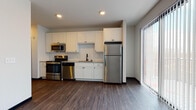 This single-floor unit in Fitchburg, Wisconsin offers a thoughtfully designed layout with modern finishes throughout. The kitchen serves as a central highlight, featuring white shaker-style cabinetry extending to the ceiling for generous storage, granite countertops, and a classic subway tile backsplash. A full suite of stainless steel appliances—including a refrigerator, range, dishwasher, and microwave—adds a sleek, contemporary feel. A large sliding glass door floods the open living and kitchen area with natural light while providing access to the outdoors.

Rich, dark hardwood-style flooring flows consistently throughout the main living areas, complementing the neutral color palette and clean lines of the space. The bedroom offers a comfortable footprint, complete with a ceiling fan, a wall-mounted HVAC unit, and ample natural light from multiple windows. An additional room features wood-tone flooring, a ceiling fan, and access to a walk-in closet with built-in shelving.

The bathroom is finished with a white vanity, granite countertop, an undermount sink with chrome fixtures, and a large mirror with a dark frame, adding a refined touch. Light tile flooring and crisp white walls complete the clean, modern aesthetic found throughout this well-appointed unit.