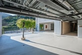 Located along Laguna Canyon Road in Laguna Beach, California, this two-story commercial building offers a substantial footprint across two well-proportioned floors. The architecture blends raw industrial elements—corrugated metal cladding, exposed ceiling systems, and steel mesh railings—with refined interior finishes, creating a striking contrast suited to creative or gallery use.

The ground floor features polished concrete floors, floor-to-ceiling black-framed glass doors, and track lighting throughout, making it highly adaptable as exhibition or retail space. Large windows flood the interior with natural light and provide views of surrounding mature trees. A refined wet bar area with dark cabinetry and dramatic stone countertops adds a sophisticated hospitality element. Glass-partitioned rooms offer flexible configurations for private showings or offices.

The upper floor continues the gallery aesthetic with exposed beam ceilings painted white, track lighting, and open lounge areas. Expansive outdoor terraces on both levels provide generous open-air space with panoramic views of Laguna Canyon's rolling, tree-covered hills. An outdoor kitchen station on the upper terrace enhances event functionality. The overall ambiance is clean, contemporary, and purposefully designed to support art presentation, creative enterprise, or experiential retail.