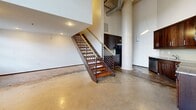 Located at 675 N Main St in downtown Winston-Salem, this two-bedroom, two-bathroom unit spans two floors with a distinct industrial-modern character. The ground floor impresses with soaring ceilings, polished concrete floors, and an open-concept layout anchored by a sleek kitchen featuring dark cabinetry, granite countertops, and stainless steel appliances. A striking open-tread staircase with a wood-and-metal railing connects the floors. Upstairs, warm hardwood flooring runs throughout both bedrooms, which are complemented by natural light from grid-pane windows. Both bathrooms feature slate tile flooring, and the primary bath includes a tub/shower combo and pedestal sink. Exposed pipes and ductwork add to the urban loft aesthetic throughout.