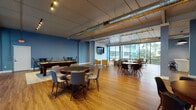 Located on Gulf Boulevard in North Redington Beach, Florida, this single-floor community and event space offers a dynamic, open-plan layout designed for both leisure and social gatherings. The interior is defined by bold blue accent walls, warm hardwood-style flooring, and exposed industrial ductwork that lends the space a modern, loft-inspired character. Track and string lighting throughout creates an inviting, versatile ambiance suitable for a range of events.

The main gathering area is generously proportioned, accommodating multiple seating arrangements including round tables with upholstered chairs, vibrant yellow lounge chairs, and high-top bar tables. A wall-mounted flat-screen TV anchors a shiplap accent wall, creating a comfortable viewing lounge area. A full-size pool table positioned on a area rug adds a recreational focal point to the space.

Floor-to-ceiling glass windows and sliding doors line one side of the room, flooding the interior with natural light and offering views of the surrounding tropical landscaping and building courtyard. The fully equipped kitchen features stainless steel appliances, white cabinetry, open shelving, and a peninsula with bar seating — ideal for catering or communal use. Structural columns punctuate the open floor plan, adding an architectural dimension to this well-appointed, multi-purpose gathering space.