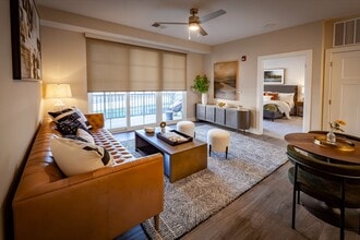 Elegant apartment living room with a chic leather sofa, modern decor, abundant natural light, and an open layout, including dining area, flowing into a cozy bedroom. - Madison at Greenwood