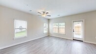 Located at 7711 Longmire Rd in Conroe, Texas, this two-story home offers a thoughtfully designed layout spread across two floors. The main level opens into a combined kitchen and living area, where the kitchen stands out with tall white cabinetry, a white subway tile backsplash, dark granite countertops, stainless steel appliances, and a central island with a sink. The living room benefits from multiple windows fitted with blinds, a ceiling fan, and light-toned luxury vinyl plank flooring that flows throughout the home, creating a bright and cohesive feel. A hallway connects the main areas seamlessly, with recessed pendant lighting guiding the way. The second floor hosts the three bedrooms, each featuring ceiling fans, generous natural light from large windows, and the same durable flooring. The spacious primary bedroom includes its own walk-in closet outfitted with built-in shelving and hanging rods for ample storage. The three bathrooms are clean and functional, with white vanities, granite countertops, dark hardware accents, and tub-shower combinations. A dedicated laundry room with a full-size washer and dryer and overhead shelving adds everyday convenience. The home presents a clean, modern aesthetic throughout with neutral tones and quality finishes.