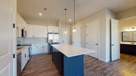 This single-floor residence at 1145 Chambers Rd in Columbus, Ohio presents a thoughtfully designed open-concept layout with contemporary finishes throughout. The kitchen serves as the centerpiece of the living space, anchored by a striking navy blue island topped with a crisp white quartz countertop and illuminated by two globe pendant lights with brass accents. White shaker-style cabinetry lines the walls, complemented by a classic subway tile backsplash and a full suite of stainless steel appliances, including a French door refrigerator, range, over-the-range microwave, and dishwasher. Rich, dark hardwood-style flooring extends throughout the main living areas, adding warmth and contrast to the neutral wall tones. The living area benefits from natural light provided by front-facing windows. Bedrooms feature plush carpet flooring; one room includes an arched window that brings in abundant daylight. The primary bathroom is appointed with a dark-toned double vanity, white quartz countertop, a large framed mirror, and a walk-in tile shower with black trim accents. An adjacent walk-in closet offers wire shelving across multiple tiers for generous storage capacity.