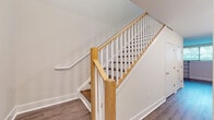 This two-story space is designed with a clean, modern aesthetic that combines practicality and style. A central staircase serves as a notable architectural feature, showcasing warm natural oak newel posts and handrails paired with crisp white balusters, all set above rich hardwood-style flooring that flows consistently throughout the main level.

The kitchen is thoughtfully laid out in a galley configuration, offering white shaker cabinetry with brushed nickel hardware, light speckled granite countertops, and a full suite of stainless steel appliances including a refrigerator, gas range, microwave, and dishwasher. Recessed lighting illuminates the space efficiently.

The bathroom presents a clean, neutral palette with white subway tile surrounding a full tub-shower combination, a white vanity with ample counter space, and light tile flooring with chrome fixtures throughout.

Additional rooms feature hardwood-style flooring, natural light from windows with blinds, and wall-mounted mini-split HVAC units for individual climate control. The overall ambiance is bright, neutral, and move-in ready, with consistent finishes tying each space cohesively together.