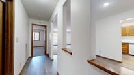 This single-floor unit offers a thoughtfully organized layout encompassing three bedrooms, two bathrooms, two living areas, and a kitchen. The hallways connect the living spaces to the bedrooms, featuring hardwood-style flooring, clean white walls with warm wood trim, and a textured ceiling. Half-wall partitions with wood ledges add a distinctive architectural detail, visually separating the living areas while maintaining an open feel. Natural light filters in through multiple windows fitted with horizontal blinds, enhancing the bright, neutral palette throughout.

The kitchen is equipped with warm oak cabinetry, a double-basin stainless steel sink, white countertops, and a stainless steel refrigerator, all set over durable hardwood-style flooring. The bedrooms feature plush carpeting, white walls with wood baseboards, and windows providing natural light. The primary bedroom includes access to an outdoor balcony. Closets feature wire shelving systems for organized storage. The bathroom includes a vanity with oak cabinetry, a large mirror, a tub-shower combination, and tile flooring. Overall, the space presents a clean, functional, and comfortable environment.