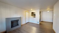 Located at 1060 Insignia Loop in Bremerton, Washington, this single-floor residence offers a thoughtfully designed layout with modern finishes throughout. The open living area serves as the heart of the home, anchored by a sleek tile-surround fireplace and durable wood-look flooring that adds warmth and continuity to the space. A pass-through window connects the living room to the kitchen, creating an open and communicative flow between the two areas.

The kitchen is well-equipped with dark wood cabinetry, crisp white countertops, a single-basin sink, and a full suite of stainless steel appliances, including a refrigerator, range, microwave, and dishwasher. Light wood-look flooring in the kitchen complements the cabinetry for a clean, contemporary aesthetic.

A separate area of the home features a glass door leading to a private balcony with outdoor views, complemented by a large window that floods the space with natural light. The bedrooms are carpeted for comfort and feature windows that bring in additional natural light, providing serene views of the surrounding neighborhood.

The bathroom is finished with wood-look flooring, dark cabinetry with a vanity mirror and overhead lighting, and a full tub-shower combination. The neutral color palette and consistent use of quality materials throughout the residence create a cohesive, modern living environment.