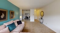 This single-floor residence offers a thoughtfully arranged layout that balances comfort and functionality. The living room is a welcoming space highlighted by a bold teal accent wall, soft carpeted flooring, and an open sightline into the adjacent dining area. The dining space features tile flooring and accommodates a full dining set, creating a natural flow for everyday living and entertaining. A console table with a decorative oval mirror adds a stylish touch near the entryway corridor.

The galley-style kitchen is outfitted with warm wood cabinetry, ample counter space, a double stainless steel sink, and a matching teal accent wall that ties the space visually to the living area. Light tile flooring and a range complete the functional kitchen setup.

The primary bedroom is generously sized, featuring plush carpet, a large window that fills the room with natural light and outdoor views, and an impressive built-in wood wardrobe unit with integrated mirrored panels and storage drawers. The second bedroom offers a quieter, neutral palette with a sliding-door closet and soft carpeting. The full bathroom includes a wood-toned vanity, medicine cabinet with overhead lighting, and tile flooring, offering a clean and practical finish.