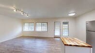 This single-floor residence offers a clean, modern aesthetic with a thoughtfully designed open-concept layout. The living area is bright and spacious, featuring wood-style laminate flooring, neutral white walls, and large multi-pane windows that invite abundant natural light. Track lighting overhead provides additional illumination, and a glass-paneled exterior door offers convenient outdoor access.

The kitchen is well-equipped and functional, showcasing white shaker-style cabinetry, dark granite-look countertops, and a full suite of stainless steel appliances including a refrigerator, electric range, and over-the-range microwave. A central island with a warm butcher block countertop adds workspace and visual interest, enhancing the kitchen's practicality.

The bedroom features wood-style flooring, a large window with an outdoor view of surrounding trees, and a reach-in closet with built-in shelving and a hanging rod, providing organized storage. The bathroom is clean and efficient, with a full-sized soaking tub and shower combination, built-in surround shelving, and chrome fixtures.

Throughout the space, the consistent use of light tones, updated flooring, and ample natural light creates a cohesive, inviting atmosphere that balances modern convenience with comfortable everyday living.