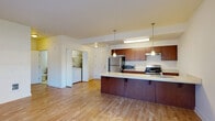 This single-floor unit offers a thoughtfully designed open-concept layout that seamlessly connects the kitchen and living areas. Light hardwood flooring flows throughout the main living spaces, creating a warm and cohesive aesthetic.

The kitchen is a standout feature, centered around a generously sized peninsula with a light-toned countertop that provides ample workspace and casual seating. Rich medium-toned wood cabinetry lines both the upper and lower sections of the kitchen, complemented by stainless steel appliances including a refrigerator, gas range, and microwave. Pendant lighting hangs above the peninsula, adding a modern touch. An adjacent in-unit laundry area houses a full-sized washer and dryer for added convenience.

The living area is spacious and bathed in natural light from large windows that offer views of the surrounding exterior. A door provides direct outdoor access, enhancing the open feel of the space.

The bedroom features hardwood flooring and a window that brings in additional natural light. The full bathroom is cleanly finished with a single-sink vanity featuring matching wood cabinetry, a large mirror, and a tub-shower combination with a sliding rail showerhead.