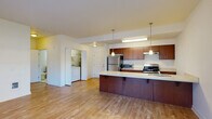 This single-floor unit offers a thoughtfully designed open-concept layout that seamlessly connects the kitchen and living areas. Light hardwood flooring flows throughout the main living spaces, creating a warm and cohesive aesthetic.

The kitchen is a standout feature, centered around a generously sized peninsula with a light-toned countertop that provides ample workspace and casual seating. Rich medium-toned wood cabinetry lines both the upper and lower sections of the kitchen, complemented by stainless steel appliances including a refrigerator, gas range, and microwave. Pendant lighting hangs above the peninsula, adding a modern touch. An adjacent in-unit laundry area houses a full-sized washer and dryer for added convenience.

The living area is spacious and bathed in natural light from large windows that offer views of the surrounding exterior. A door provides direct outdoor access, enhancing the open feel of the space.

The bedroom features hardwood flooring and a window that brings in additional natural light. The full bathroom is cleanly finished with a single-sink vanity featuring matching wood cabinetry, a large mirror, and a tub-shower combination with a sliding rail showerhead.