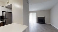 This single-floor residence offers a clean, modern aesthetic throughout, with thoughtfully selected finishes that create a cohesive and comfortable living environment. The living room serves as the centerpiece of the home, showcasing light gray luxury vinyl plank flooring, neutral-toned walls, and a striking black-tiled fireplace with a white mantle. A sliding glass door fitted with vertical blinds allows natural light to fill the space and provides access to the outdoors. The kitchen is efficiently designed with dark wood cabinetry, white countertops, and a full suite of stainless steel appliances including an electric range, over-the-range microwave, and a sink with ample counter space. The bedroom is carpeted for comfort and features a window dressed with horizontal blinds, allowing soft natural light to filter in. The bathroom is finished with gray tile flooring, a modern vanity with dark wood cabinetry, and a full bathtub/shower combination accented by a striking multi-toned tile surround. An entryway area with durable wood-look flooring connects the rooms and provides practical transition space. Overall, the residence presents a well-maintained, move-in-ready interior with a neutral color palette and updated finishes throughout.