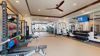 Located at 4455 Condor Dr in Hilliard, Ohio, this professionally appointed fitness center offers a spacious, single-floor layout designed to accommodate a full range of workout needs. The space is organized into distinct training zones, each thoughtfully equipped to support varied fitness goals.

The strength training area features a comprehensive free weights section with a full dumbbell rack, multiple adjustable benches, a power rack, and a TKO functional trainer complete with kettlebells and TRX suspension straps. Floor-to-ceiling mirrors line the walls, enhancing the sense of openness and allowing users to monitor their form during lifts.

A dedicated cardio zone lines the perimeter, featuring stationary bikes, elliptical trainers, and treadmills positioned beside large, black-framed windows that invite abundant natural light and outdoor views of the surrounding community. The bright, airy atmosphere is further elevated by recessed lighting throughout.

Ceiling fans with rich dark wood accents are mounted within tray ceilings that add architectural refinement to the space. The flooring transitions between durable rubberized surfaces in high-traffic workout areas and smooth, light-toned flooring elsewhere, offering both functionality and a clean aesthetic. The overall design strikes a balance between modern style and practical utility, making this fitness center a standout amenity.