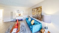 This single-floor residence offers a thoughtfully designed layout that balances comfort and functionality across its key living areas. The living room serves as the heart of the home, featuring wood-look flooring, a textured ceiling, and ample wall space for artwork — creating a warm and inviting atmosphere. Natural light filters in through vertical-blind windows, lending the space an open, airy feel. Adjacent to the living area, the dining space accommodates a round table with seating for four, accented by a ceiling fan with light fixture overhead. The kitchen is efficiently arranged with white cabinetry, light countertops, and stainless steel appliances including a gas range with overhead microwave and a full-size refrigerator. A window above the counter brings in additional natural light. The bedroom is generously sized with plush carpeting, textured ceiling, and a wide window for natural illumination — providing a quiet retreat. The bathroom features a long, elongated vanity with a white countertop, undermount sink, and a large mirror above, all finished with wood-look tile flooring that carries a cohesive design aesthetic throughout the unit. Together, these spaces create a clean, modern, and comfortable living environment.