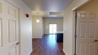 Located at 5920 Cromo Dr in El Paso, TX, this single-story unit offers a well-designed open-concept layout with consistent dark hardwood-style flooring throughout. The entryway welcomes residents with a pendant light fixture and flows seamlessly into the main living area, which benefits from natural light streaming through a sliding glass door.

The kitchen serves as a focal point of the space, featuring a large center island with an integrated sink and light countertops that contrast elegantly with dark navy cabinetry. Stainless steel appliances, including a refrigerator, electric range, and built-in microwave, complete the functional cooking space. A track lighting system and additional pendant lights illuminate the kitchen and adjacent living area.

The bedroom is a well-proportioned room with a ceiling fan, a window offering views of the surrounding El Paso landscape, and the same rich hardwood-style flooring found throughout the unit. The bathroom includes a full soaking tub with a tiled surround in a neutral stone-like finish, hardwood-style flooring, and a built-in shelving unit for added storage convenience. The overall design balances practicality with modern aesthetics, making this a clean and functional living space.