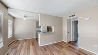 This single-story residence offers a practical and cohesive layout connecting the main living areas through an open floor plan. Wood-look plank flooring runs throughout the living, dining, and bedroom spaces, providing a consistent and clean aesthetic. The textured ceiling is present throughout, and neutral warm-beige walls create a calm, understated ambiance.

The kitchen is configured as a galley-style space and is accessible from the living area via a peninsula counter with a gray laminate surface and a built-in sink. Gray cabinetry lines both sides of the kitchen, offering generous storage, while white appliances — including a refrigerator, gas range, and dishwasher — complete the setup. A pass-through opening connects the kitchen visually to the living space.

The living area is open and well-proportioned, featuring a ceiling fan, a central HVAC vent, and a front entry door flanked by a window fitted with horizontal blinds, allowing natural light into the space.

The bedroom is a quiet, carpeted-free room with the same wood-look flooring and neutral walls. The bathroom includes a walk-in tile shower with grab bars, a toilet, and a vanity with a gray countertop and mirror.