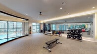 Located at 2925 Buford Dr in Buford, GA, this fitness center is a thoughtfully designed, single-floor facility that combines functionality with a polished, modern aesthetic. The space is anchored by a generously sized open workout area finished with textured, neutral-toned carpet tiles that provide both comfort and durability underfoot.

Floor-to-ceiling mirrors line one wall, amplifying the sense of space and allowing users to monitor their form during exercise. Recessed lighting is complemented by warm cove lighting along the ceiling's tray detail, creating a bright yet inviting atmosphere. A ceiling fan adds practical airflow to the workout environment.

The facility is well-stocked with a comprehensive range of free weights, including a full rack of dumbbells and a colorful, organized set of kettlebells. Adjustable benches, a cable resistance machine, and medicine ball storage complete the equipment offerings. Wall-mounted flat-screen televisions provide entertainment throughout workouts.

Large windows along the exterior walls invite abundant natural light and offer views of the surrounding area. The fitness center is accessed through sleek glass doors with stainless steel hardware, connecting to an elegant curved corridor and a multi-level common area featuring an open staircase and expansive floor-to-ceiling windows.