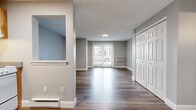 Located at 141 Sea St in Quincy, MA, this single-floor unit offers an efficient and well-designed layout comprising a living room, bathroom, and entrance. The space is finished with durable hardwood-style flooring throughout, complemented by neutral gray walls and crisp white baseboards that create a clean, modern aesthetic.

The living room is the centerpiece of the unit, featuring a sliding glass door that fills the room with natural light and provides direct access to an outdoor area with views of the surrounding neighborhood. A wall-mounted air conditioning unit ensures year-round comfort, while a baseboard heating system runs along the perimeter of the room. A pass-through window connects the living area to the kitchen space, adding an open, communicative feel between rooms.

The entrance area includes a large double-door closet with six-panel doors, offering generous built-in storage. The bathroom is outfitted with a full soaking tub enclosed by clean white subway-style tiles and chrome fixtures, delivering a simple and functional design.

Throughout the unit, consistent use of light tones, smooth ceilings, and well-maintained finishes contribute to a bright and cohesive living environment. This space is well-suited for those seeking a straightforward, low-maintenance residence in the Quincy area.