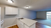 Located at 401 E Magnesium Rd in Spokane, WA, this two-bedroom, one-bathroom unit is thoughtfully laid out across a single floor. The open-concept kitchen and living area serves as the heart of the home, where a peninsula with a light granite-style countertop and an integrated sink separates the kitchen from the living space. The kitchen is equipped with white cabinetry, a white refrigerator, electric range, and microwave. Hardwood-style flooring runs throughout the kitchen and entry areas, adding warmth and easy maintenance. The spacious living room features plush carpeting, a textured ceiling, a wood-paneled accent wall, and a sliding glass door that opens to a private balcony with outdoor views. Baseboard heating is present throughout the unit. The two bedrooms are carpeted and offer a quiet retreat, each with closet storage featuring hanging rods. One bedroom includes a wall-mounted AC unit and a window allowing natural light. The bathroom is clean and functional, featuring a full-size soaking tub with an overhead shower and white surround. A hallway connects the private areas of the unit, and two closets provide ample additional storage. The layout is efficient and practical, making excellent use of the available space.