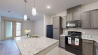 This one-bedroom, one-bathroom unit in Dallas, Texas offers a thoughtfully designed layout that maximizes its compact footprint. The open-concept kitchen is a standout feature, showcasing granite countertop surfaces on a spacious peninsula island, rich dark-toned cabinetry, and black stainless steel appliances including a refrigerator, range, and built-in microwave. Pendant lighting over the island adds a refined touch, while light wood-style flooring flows throughout the main living area, contributing to a bright and modern aesthetic. The bedroom is a comfortable retreat, finished with soft carpeting, a ceiling fan with integrated lighting, and a large window fitted with blinds that invites natural light and provides views of the surrounding community. The bathroom continues the cohesive design language with matching dark cabinetry, granite countertops, a double-sink vanity, a large framed mirror, and a walk-in shower. A dedicated closet provides practical storage. Clean white walls and consistent finishes throughout create a unified, contemporary living environment suited for comfortable everyday living.