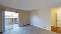 This single-floor space offers a clean and functional layout designed with everyday comfort in mind. The main living area is finished with wall-to-wall carpet in a neutral gray tone, providing a soft and practical underfoot surface. Warm beige walls create a neutral backdrop throughout, complemented by crisp white baseboards and a textured ceiling that adds subtle visual interest overhead.

A prominent sliding glass door dominates one wall, flooding the space with natural light and offering direct access to a private balcony. The balcony features slatted railing and overlooks a lush, tree-lined outdoor setting, making it an inviting spot for relaxation. The sliding door is fitted with a simple overhead track and allows for an easy transition between the interior and exterior.

Integrated floor vents provide climate control throughout the space, and recessed electrical outlets are conveniently positioned along the baseboards. The overall ambiance is bright, understated, and move-in ready, with a straightforward design that offers a versatile canvas for personalization. The space is well-suited for those seeking a low-maintenance environment with a connection to the outdoors.