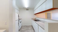 Located at 115 W Limberlost Dr in Tucson, Arizona, this 2-bedroom, 1-bathroom unit offers a practical and well-organized single-floor layout. The combined kitchen and living area forms the heart of the home, with the kitchen featuring white cabinetry extending to the ceiling for ample storage, laminate countertops, a double-basin sink, and white appliances including a range and refrigerator. Wood-look flooring runs throughout the main living areas, lending a clean, cohesive aesthetic. The living room is a comfortable open space with a ceiling fan and a sliding glass door fitted with vertical blinds, allowing natural light to filter in while providing access to the outdoors. Both bedrooms are carpeted for warmth and comfort, with the primary bedroom offering a closet with a sliding door and built-in rod and shelf. A dedicated walk-in style closet provides additional storage. The bathroom includes a single-sink vanity with a mirrored medicine cabinet, a tub/shower combination with tile surround and safety grab bar, open shelving, and wood-look flooring. A hallway connects the main living areas to the bedrooms, and in-unit laundry connections add everyday convenience to this straightforward Tucson residence.