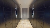 This single-floor package room is designed to provide a streamlined and secure solution for parcel management. The space is lined on both sides with large, dark-toned smart package lockers, each unit equipped with illuminated touchscreen interfaces that allow residents or users to retrieve deliveries conveniently and independently. The lockers extend the full length of the corridor-style room, offering substantial storage capacity across multiple compartment sizes to accommodate parcels of varying dimensions. The room is anchored by a classic raised-panel gray door at the far end, fitted with a keypad access control system, reinforcing the security-focused design of the space. Underfoot, a distinctive geometric parquet-style wood floor adds a refined aesthetic contrast to the utilitarian purpose of the room, featuring a light natural wood tone with an intricate pattern that elevates the overall design. Recessed ceiling lighting provides clean, even illumination throughout the narrow passage. The combination of functional smart-locker technology, secure entry, and polished finishes reflects a thoughtfully designed amenity space built for modern convenience.