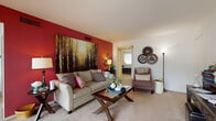 This single-floor residence offers a thoughtfully designed layout that balances comfort and functionality across its key living spaces. The living room serves as the heart of the home, anchored by a bold crimson accent wall adorned with a large nature-inspired canvas painting. Soft carpeting, a glass-top coffee table, and a sliding glass door that floods the room with natural light and provides access to an outdoor patio create an inviting, open atmosphere. A dedicated workspace area with a dark wood desk and storage rounds out the living space. The kitchen features rich dark wood cabinetry, generous counter space, and a stainless steel sink, offering a practical and efficient cooking environment. The primary bedroom is a serene retreat with plush carpeting, a ceiling fan, and a wide window that lets in natural light. Dual sliding closet doors provide substantial storage. A second bedroom, finished in warm tones with its own closet and window, offers comfortable accommodations. The bathroom is laid out in a corridor style, featuring classic mosaic tile flooring, a long vanity with a single-basin sink, and a large mirror, with convenient access to the adjoining rooms.