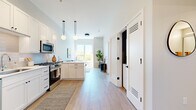 Located at 153 E First St in Elmhurst, IL, this thoughtfully designed one-bedroom, one-bathroom residence offers a well-organized, single-floor layout that maximizes every inch of its compact footprint. The open-concept kitchen and living area form the heart of the home, where light wood-tone flooring, white walls, and soaring ceilings create a clean, airy atmosphere. The kitchen is outfitted with white shaker-style cabinetry extending to the ceiling, a white tile backsplash, stainless steel appliances including a gas range, built-in microwave, dishwasher, and full-size refrigerator, and a double sink beneath pendant globe lighting. The living area benefits from a large picture window that fills the space with natural light and frames outdoor greenery. A dedicated in-unit stacked washer and dryer is conveniently tucked near the hallway. The bedroom features plush carpet, generous wall space, and a walk-in closet with built-in shelving. The bathroom includes a white shaker vanity with ample drawer storage, a large framed mirror with lighted strip, and light wood-look tile flooring, maintaining the home's consistent modern aesthetic throughout.