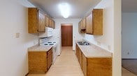 Located at 3000 S Louise Ave in Sioux Falls, South Dakota, this single-floor unit offers a practical and well-organized layout across several distinct living spaces. The living area features a combination of light hardwood-style flooring and carpet, with a ceiling fan providing comfort and a sliding glass door that opens to a balcony, allowing natural light and outdoor views to flow into the space. A wall-mounted air conditioning unit ensures year-round climate control.

The bedrooms are carpeted for comfort and each features a ceiling fan with integrated lighting, a window with views of surrounding greenery, and baseboard heating. The windows allow ample natural light to brighten each room throughout the day.

The galley-style kitchen is efficiently designed with warm wood cabinetry lining both sides, offering generous storage space. It is equipped with a white electric range, overhead microwave, refrigerator, and a double-basin sink with a nearby closet providing additional storage.

The bathroom is finished with tile flooring and includes a full tub-shower combination, wood cabinetry above the toilet for storage, and a vanity with countertop space. Textured ceilings are consistent throughout the unit, contributing to its classic residential character.
