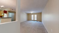 This single-floor residence offers a practical and comfortable layout across two bedrooms and two bathrooms. The spacious living room serves as the heart of the home, featuring soft wall-to-wall carpeting, warm neutral tones, a ceiling fan, and a set of French doors that invite natural light and provide outdoor access. A partial dividing wall separates the living area from the kitchen, creating an open yet defined flow between spaces.

The galley-style kitchen is efficiently designed with warm wood cabinetry lining both sides, light countertops, a double basin sink, and wood-look vinyl flooring. White appliances including a refrigerator and range complete the setup. Directly accessible from the kitchen is a dedicated laundry room housing a full-size washer and dryer.

Both bedrooms are generously proportioned, finished with plush carpet and neutral wall tones. The primary bedroom offers ample space, while the secondary bedroom features a ceiling fan and a window with a garden view. Each room provides a calm, understated atmosphere suited for rest and relaxation.

The two bathrooms are finished with wood-look tile flooring, warm wood vanity cabinetry, and clean white fixtures including a soaking tub. A hallway connects the private areas of the residence, and a closet provides additional storage. The layout throughout is cohesive and thoughtfully arranged.