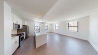 This contemporary single-floor residence offers a thoughtfully designed open-concept layout that seamlessly connects the kitchen and living areas. The kitchen is a standout feature, equipped with stainless steel appliances including a French door refrigerator, built-in microwave, and electric range. White shaker-style cabinetry with gold hardware extends to the ceiling, complemented by a generous white quartz island that doubles as a breakfast bar. Stylish globe pendant lights hang above, adding a modern touch to the space. The expansive living area is bathed in natural light streaming through multiple black-framed windows that frame urban skyline views, creating a bright and airy atmosphere throughout. Neutral-toned flooring flows through the main living spaces, while plush carpet adds comfort to the bedrooms. Each bedroom is well-proportioned, offering ample space and city views through large windows. The unit includes two bathrooms, both featuring classic black-and-white hexagonal mosaic tile flooring, white vanities with undermount sinks, and clean, minimalist finishes. One bathroom includes a walk-in glass-enclosed shower, while both offer bright, well-lit mirror arrangements. The overall design aesthetic is clean and contemporary, with a neutral palette that creates a versatile and welcoming environment.