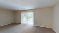 This single-floor residence offers a well-organized layout designed for comfortable everyday living. The living room is a generously sized, open space finished with neutral wall-to-wall carpeting and a textured ceiling. A large sliding glass door dressed with vertical blinds fills the room with natural light and provides direct access to an outdoor balcony, offering pleasant views of surrounding greenery.

Adjacent to the living area is a dedicated dining space, distinguished by a chandelier overhead and white paneled wainscoting along the wall, adding a subtle decorative touch. A folding door nearby leads to a utility closet with washer/dryer hookups, adding functional convenience.

The kitchen features a galley-style configuration with wood-look vinyl flooring, white cabinetry, dark granite-style countertops, a double basin sink, and white appliances including a range and refrigerator, providing efficient use of the available space.

The bedroom is spacious and carpeted, featuring a window with blinds that brings in natural light. A full bathroom includes a tiled tub/shower combo, toilet, and vanity with wood-look flooring, maintaining a clean and practical aesthetic throughout.