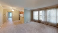This single-floor residence offers a practical and comfortable layout designed for everyday living. The open-concept living and dining area is finished with soft neutral carpeting and sage-green accent walls, creating a calm and welcoming atmosphere. A ceiling fan with integrated lighting serves the space, while large sliding doors dressed with vertical blinds invite generous natural light and offer views of the surrounding greenery. Crown molding runs throughout, adding a polished architectural detail to each room.

The kitchen is thoughtfully arranged in an L-shaped configuration, featuring warm oak cabinetry with ample upper and lower storage, white laminate countertops, a stainless steel sink, and white appliances including a refrigerator and gas range. A pass-through counter connects the kitchen to the living area, enhancing the open flow of the space. A window above the sink brings in additional natural light.

The bedroom is a generously sized, carpeted room finished in warm beige tones, with multiple windows dressed in vertical blinds that provide both natural light and privacy. Crown molding continues here, maintaining a consistent and cohesive design throughout the home.

The bathroom is finished with white tile flooring and tiled walls surrounding a full soaking tub and shower combination. Built-in cabinetry above the toilet provides convenient storage, and a window with vertical blinds allows for natural ventilation and light.