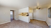 Located at 3616 Galley Rd in Colorado Springs, Colorado, this single-floor unit offers a straightforward and functional layout designed for comfortable everyday living. The open-concept living area flows seamlessly into the kitchen, which is defined by a white peninsula counter that doubles as a breakfast bar. The kitchen is well-equipped with abundant white cabinetry reaching toward the ceiling for generous storage, white appliances including a refrigerator and range, a double sink, and wood-look vinyl flooring that adds warmth and durability. A ceiling fan with integrated light fixture serves the adjoining living space, which features neutral carpet throughout. The bedroom wing includes a well-sized primary bedroom with double closets providing excellent storage, along with a secondary bedroom or flexible room. Both bedrooms are finished with plush carpet, neutral wall tones, and baseboard heating units. Natural light filters in through multiple windows fitted with blinds. The overall palette of whites and warm neutrals throughout the unit creates a clean, cohesive atmosphere. The single-story layout ensures easy accessibility, and the practical design makes efficient use of the available space.