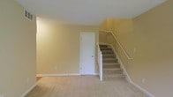 This two-floor home presents a straightforward and functional layout designed for comfortable everyday living. The main level features wall-to-wall carpeting in a neutral beige tone, contributing to a warm and quiet atmosphere throughout. The walls are finished in a soft, creamy yellow hue that reflects light and lends a welcoming feel to the interior spaces.

A white interior door on the main floor provides access to an additional room or utility space, adding to the home's practicality. The staircase, centrally positioned, connects the two floors and is finished with matching beige carpet treads and a clean white wood banister with a handrail — a classic design choice that complements the overall aesthetic of the home.

White baseboards run along the perimeter of the main level, providing a clean contrast against the carpeted flooring and painted walls. The ceiling is smooth and painted white, helping to maintain a sense of openness in the space. Overall, the interior carries a neutral, move-in-ready character, offering a blank canvas well-suited for a variety of furnishing styles and personal touches.
