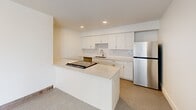 Located at 835 Van Buren in Fort Wayne, Indiana, this one-bedroom, one-bathroom unit offers a thoughtfully designed layout within a compact, efficiently utilized footprint. The building's striking exposed red brick exterior reflects its historic character, while the interior has been finished with clean, contemporary details throughout.

The kitchen is a standout feature, outfitted with white shaker cabinetry, light quartz countertops, a subway tile backsplash, stainless steel appliances including a refrigerator and range, and a central peninsula that provides additional prep and dining space. The speckled terrazzo-style flooring runs throughout the living areas, lending a cohesive and durable finish.

The bedroom is a well-proportioned, bright space with a window framing outdoor views, soft carpeted flooring, a closet with bi-fold doors, and a wall-mounted mini-split HVAC unit for personalized climate control.

The bathroom is elegantly appointed with large-format marble-look tile surrounding a soaking tub and shower combo, brushed gold fixtures, and a built-in niche for storage.

A private outdoor deck is a defining highlight of this unit, offering panoramic views of the Fort Wayne skyline and surrounding neighborhood, enclosed by iron railings against the building's classic brick façade — an ideal space for outdoor relaxation.