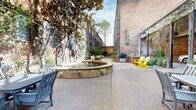 This Pool Courtyard in Dallas, TX, offers a serene retreat within an urban setting. The space is characterized by its thoughtful landscaping and architectural elements that blend nature with industrial charm. Mature trees line the concrete pathways, providing natural shade and a sense of established greenery. The courtyard is flanked by historic brick buildings, their large industrial windows reflecting the area's past while allowing ample natural light.

The space features a mix of hardscaping and softscaping. Concrete walkways are bordered by carefully tended plant beds filled with a variety of shrubs and small trees. Gravel areas add texture and aid in drainage. Colorful Adirondack chairs in vibrant yellow and teal provide comfortable seating options throughout the courtyard, encouraging relaxation and social interaction.

A black metal gate offers a sense of privacy and exclusivity to the area. The courtyard's design incorporates both open spaces for gatherings and more intimate nooks for quiet contemplation. Climbing vines on some of the brick walls soften the industrial aesthetic and add to the garden atmosphere.

This well-maintained outdoor space serves as a delightful amenity for the surrounding buildings, offering residents and visitors a peaceful escape from the urban environment. The Pool Courtyard successfully marries the area's industrial heritage with modern landscaping techniques, creating an inviting and refreshing urban oasis.