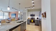 This thoughtfully designed 2-bedroom, 2-bathroom residence offers a seamless single-story open-concept layout that connects the kitchen, dining, and living areas. The contemporary kitchen is a standout feature, boasting granite countertops, two-tone cabinetry with gray lower cabinets and white uppers, stainless steel appliances including a range, microwave, refrigerator, and dishwasher, and a large island with a double sink and pendant lighting. Track lighting throughout the kitchen and living areas adds a modern touch. Light wood-style flooring runs through the main living spaces, creating a warm and cohesive feel. The dining area comfortably accommodates a full table and chairs and flows naturally into the living room. The primary bedroom features plush carpeting, a ceiling fan, large windows that invite natural light, and access to a spacious en-suite bathroom with a dual-sink granite vanity, soaking tub with marble-tile surround, and wood-style flooring. The second bedroom is equally well-lit with generous window coverage. Both bathrooms mirror each other in their refined finishes. Each bedroom is paired with a walk-in closet equipped with wire shelving and built-in storage. The entryway is welcoming with wood-style flooring and a sidelight window at the front door.
