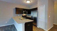 This two-floor residence offers a thoughtfully designed layout that balances functionality and modern style. The kitchen serves as a standout feature, showcasing rich, dark cabinetry that provides ample storage alongside striking light granite countertops that offer generous prep space. A peninsula with an undermount sink extends the counter area and creates a natural division between the kitchen and adjacent living spaces, making it ideal for casual dining or entertaining. Stainless steel appliances, including a French door refrigerator with an in-door water and ice dispenser, a range with an electric cooktop, and an over-the-range microwave, complete the contemporary kitchen ensemble. Warm hardwood-style flooring flows throughout, grounding the space with a sense of continuity and warmth. The neutral wall tones complement the bold cabinetry, creating a clean and balanced aesthetic. Flush-mount ceiling lighting provides consistent illumination, while white panel doors and crisp trim add a classic finishing touch. Spanning two floors, the home offers defined living areas that provide both comfort and practicality, making it a versatile and inviting space suited to a variety of lifestyles.