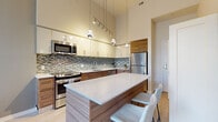 This well-appointed one-bedroom, one-bathroom residence in Silver Spring, Maryland, offers a thoughtfully designed open-concept layout with soaring ceilings that lend a sense of spaciousness beyond its compact footprint. Light hardwood flooring runs throughout, complementing the modern aesthetic.

The kitchen is a standout feature, showcasing warm walnut cabinetry paired with crisp white upper cabinets, a mosaic tile backsplash, quartz countertops, and a generous island with bar seating. Stainless steel appliances and pendant lighting complete this chef-inspired space with impressive vertical ceiling height.

The living room benefits from floor-to-ceiling windows that flood the area with natural light and frame views of mature trees outside. A wall-mounted TV, sleek media console, and sectional seating arrangement make this an inviting gathering space.

The bedroom is a serene retreat featuring large windows with verdant tree views, light hardwood floors, and clean, neutral walls that create a calm atmosphere.

The bathroom is finished with wood-grain tile flooring, a dark floating vanity with a white quartz countertop, and a tiled tub-shower combination with mosaic accent detailing.

Located at 180 High Park Ln, this residence combines contemporary design with functional living in a desirable Silver Spring location.