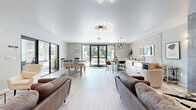 This thoughtfully designed single-floor amenity space seamlessly blends comfort, functionality, and contemporary style. The open-concept layout flows effortlessly between distinct zones, all unified by light-toned hardwood flooring and a neutral, calming palette of soft grays and whites.

The lounge area anchors the space with plush seating arrangements, including leather sofas and accent chairs, centered around a striking floor-to-ceiling tiled fireplace wall that serves as a dramatic focal point. A wall-mounted flat-screen television complements the relaxed seating nook near the main entrance, which features sleek black-framed glass doors that invite natural light throughout.

Adjacent to the lounge, the entertainment zone houses a solid wood pool table and additional casual seating, while a glass-walled meeting room — clearly labeled "MTG. RM" — provides a private, professional workspace with full outdoor views.

The kitchen and wet bar area is a standout feature, highlighted by a textured mosaic tile accent wall, a marble-topped island with bar seating, pendant lighting, stainless steel appliances, and a beverage cooler. A statement sunburst chandelier overhead adds a sculptural touch. Large French doors open directly to an outdoor patio, blurring the boundary between interior and exterior and flooding the space with greenery views and ample natural light throughout.
