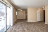This single-floor residence offers a practical and comfortable layout designed for everyday living. The open living area is generously sized, featuring warm beige walls, plush wall-to-wall carpeting, and a textured ceiling. A ceiling fan provides year-round comfort, while a sliding glass door leads to an outdoor balcony, filling the space with natural light and offering pleasant exterior views. The living area connects seamlessly to the kitchen, which is outfitted with rich oak cabinetry, light granite-style countertops, a double-basin sink, and a gas range with oven — all set atop durable hardwood-style flooring. The unit includes multiple bedrooms, each carpeted and finished in neutral tones. The bedrooms feature dedicated closets with sliding or hinged doors, providing ample storage, and windows that invite natural light. One bedroom offers dual closets for added convenience. The bathroom is well-appointed with an oak vanity, granite-style countertop, a large wall mirror, a full tub-shower combination with a white surround, and hardwood-style flooring that ties the space together cleanly. Throughout the unit, consistent warm neutral tones and functional design elements create a cohesive and inviting atmosphere.
